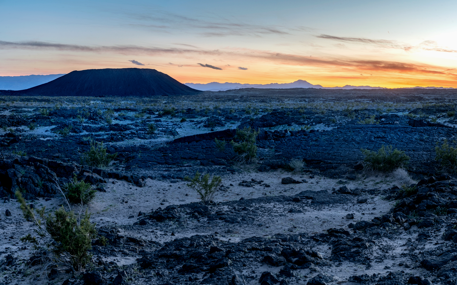 Dark volcanic crater rising from Mojave Desert scrub near Amboy